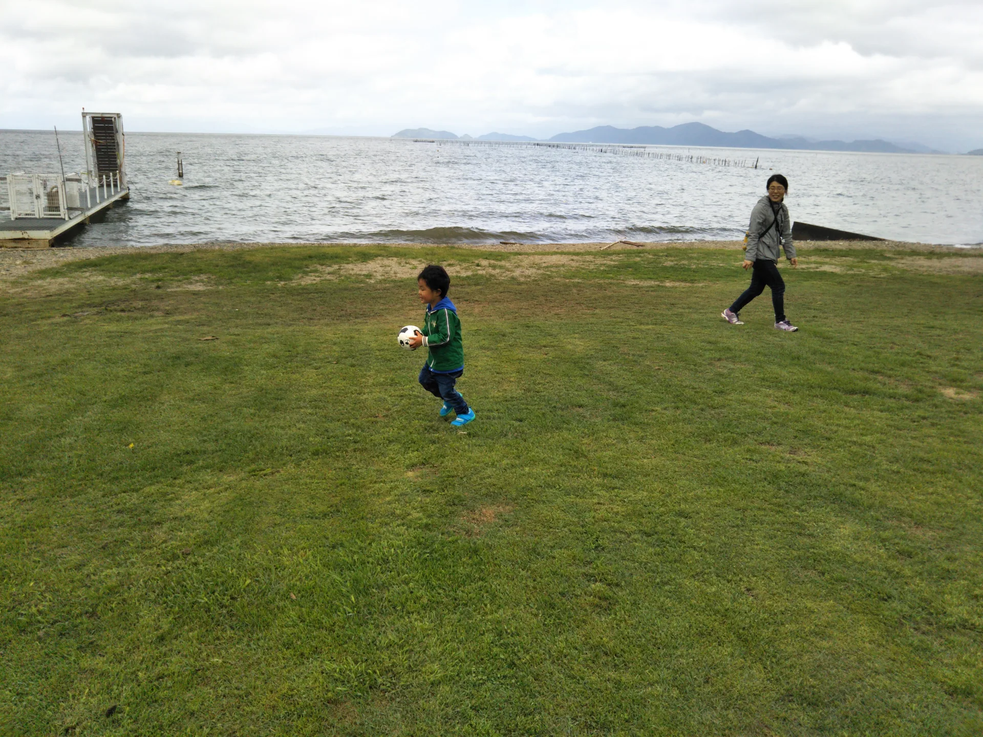 湖前の芝生でボールを持つ子供と、そばにいる大人